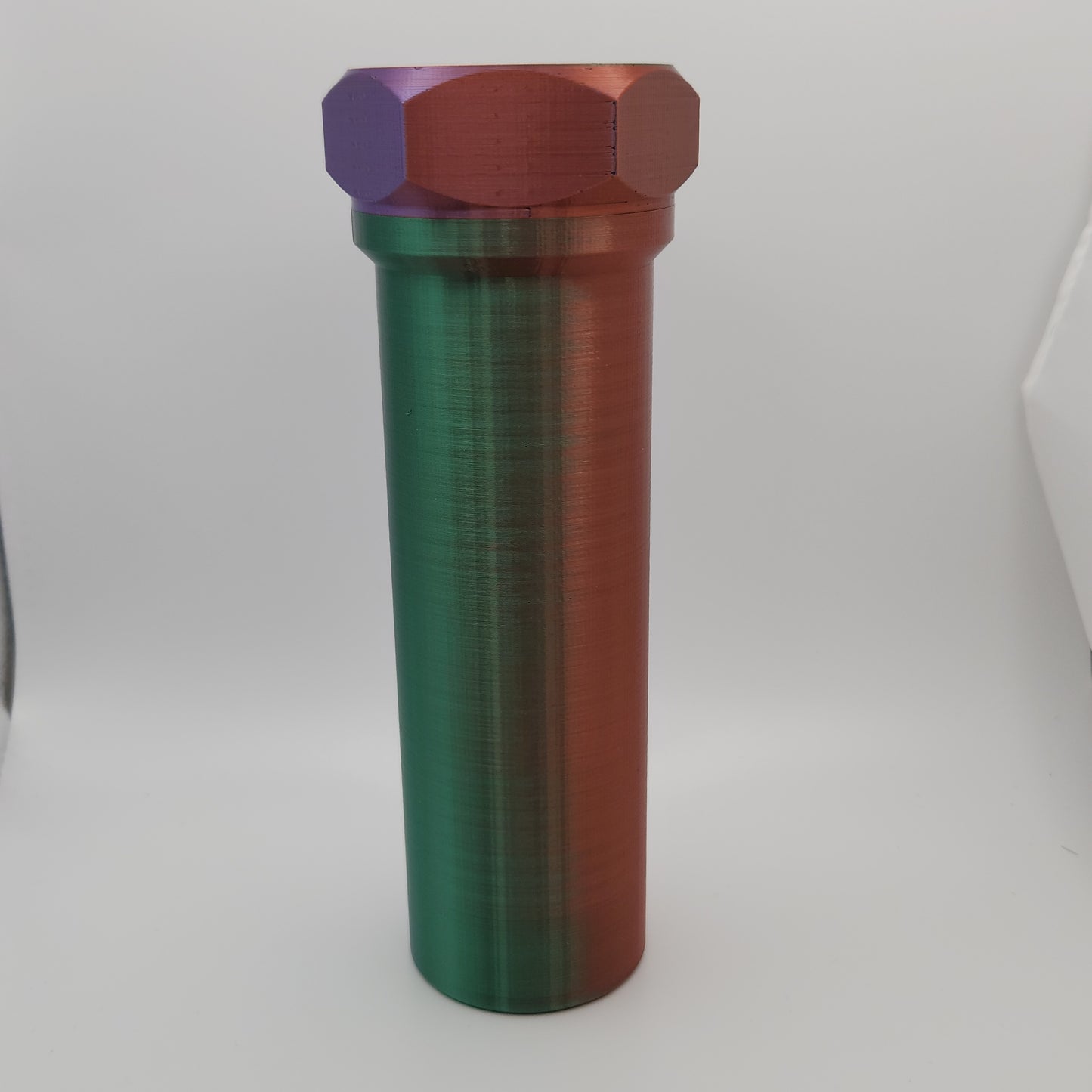 A cylindrical container with a gradient color scheme transitioning from purple to green to red. The container has a hexagonal cap and is standing upright against a white background. The surface is smooth with a metallic sheen.