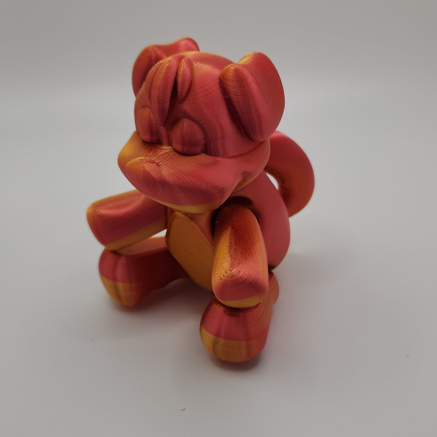A 3D-printed dog figurine in a mix of red and gold colors, shown sitting upright. The dog has a rounded, smooth body with detailed facial features, including a prominent snout and closed eyes, giving it a cute and relaxed expression.