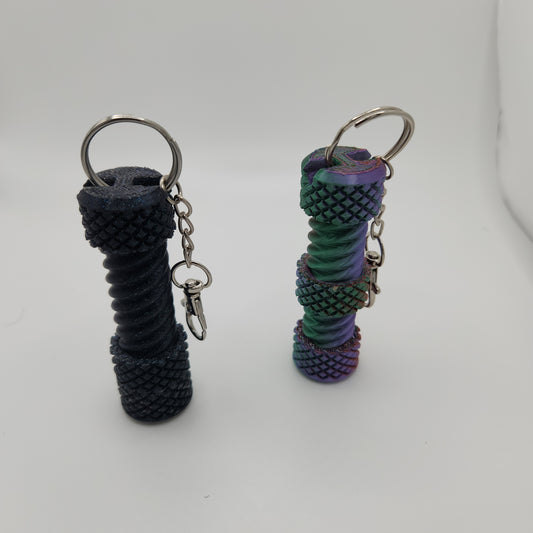 An image showing two cylindrical fidget bolts standing upright side by side. The bolt on the left is black with a glittery finish, while the one on the right has a gradient color scheme transitioning between purple, green, and rainbow hues. Both bolts have keyrings attached at the top.
