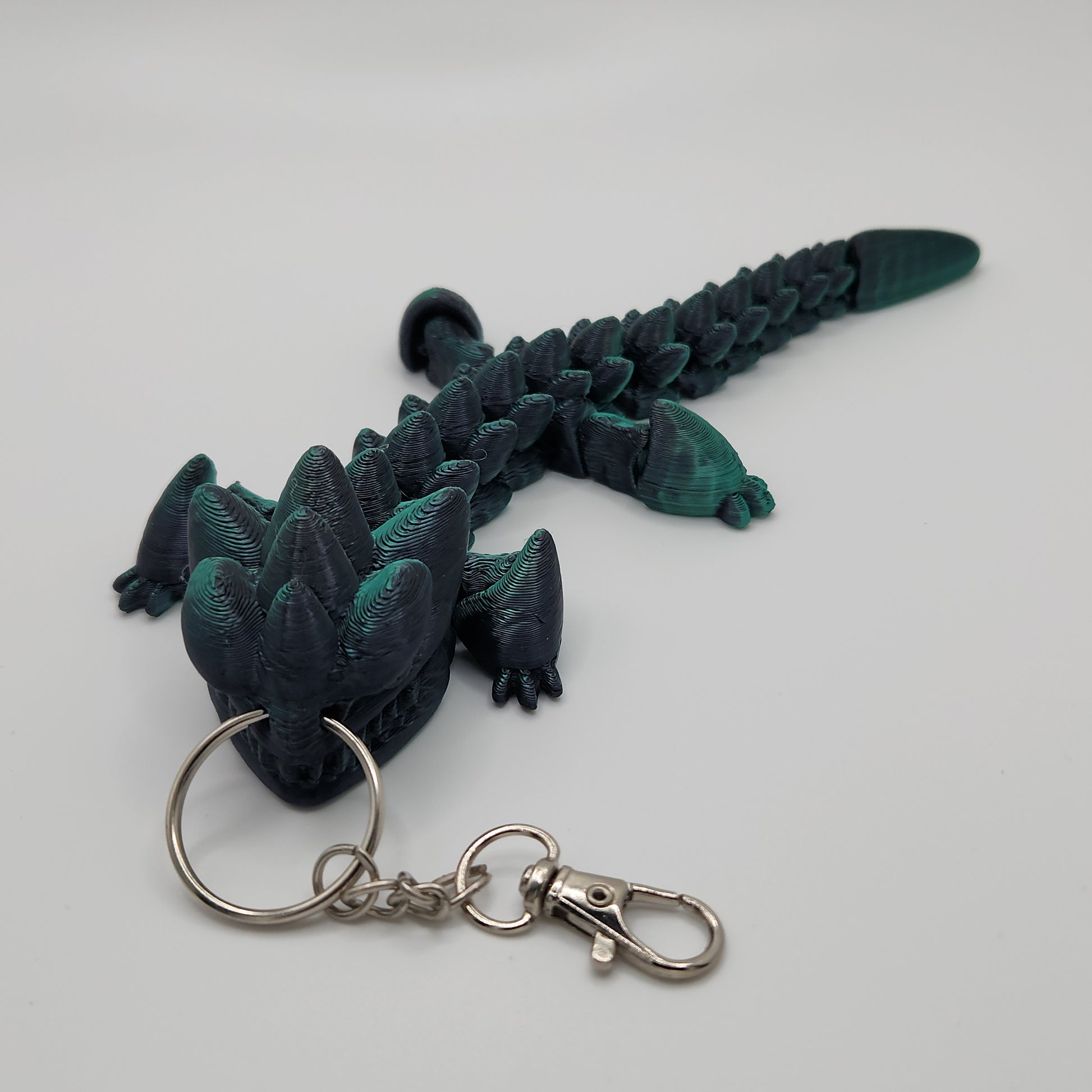 A side view of the black and teal articulated dragon keychain stretched out, displaying its full length and detailed scales.