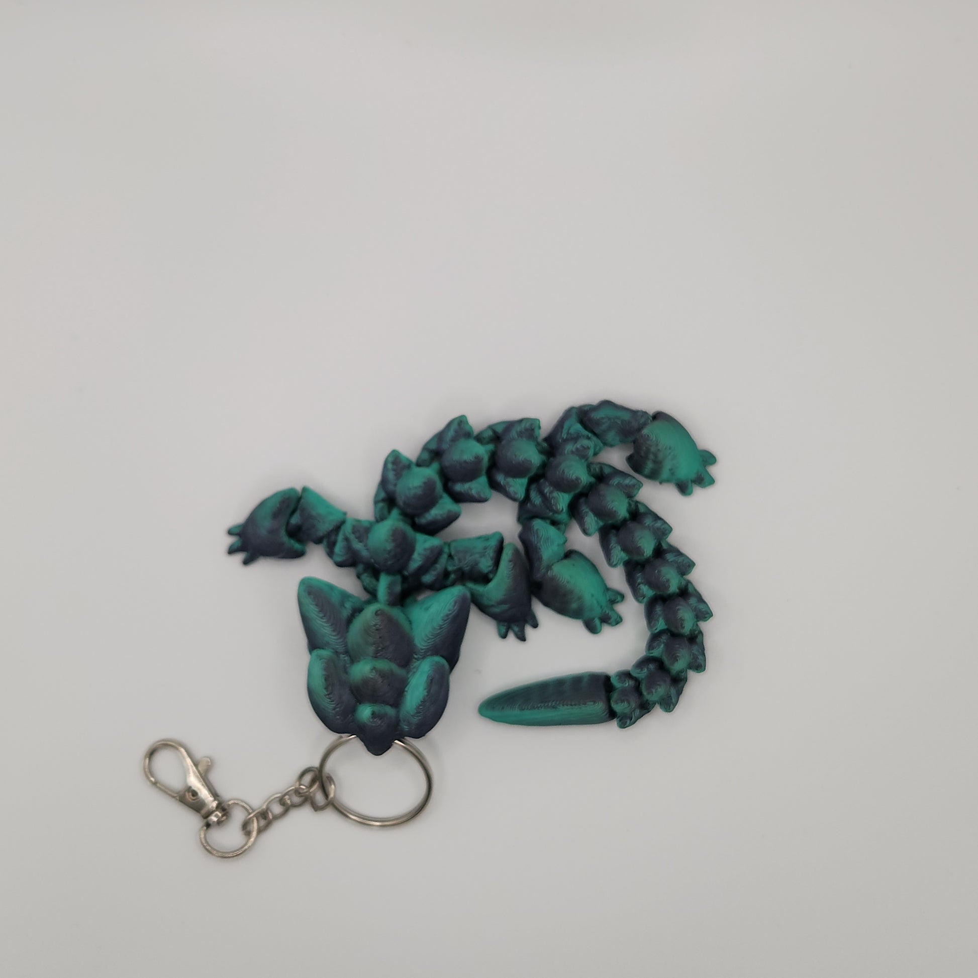 Top-down view of the black and teal articulated dragon keychain, showing its segmented body and attached metal keychain.