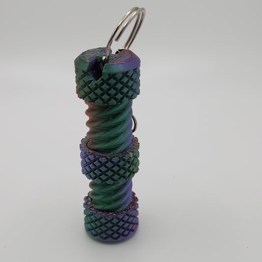 A close-up image of a cylindrical fidget bolt with intricate, textured patterns. The bolt features a gradient color scheme that transitions between purple, green, and rainbow hues. It has a keyring attached at the top, making it easy to carry.